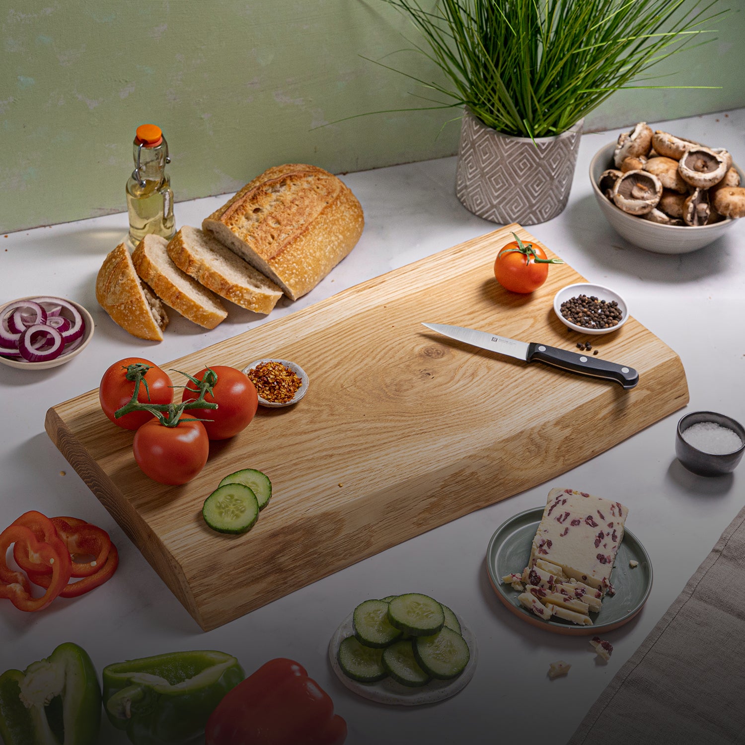 Oak live edge wooden chopping board with sliced bread, vegetables, and a knife on a kitchen counter.