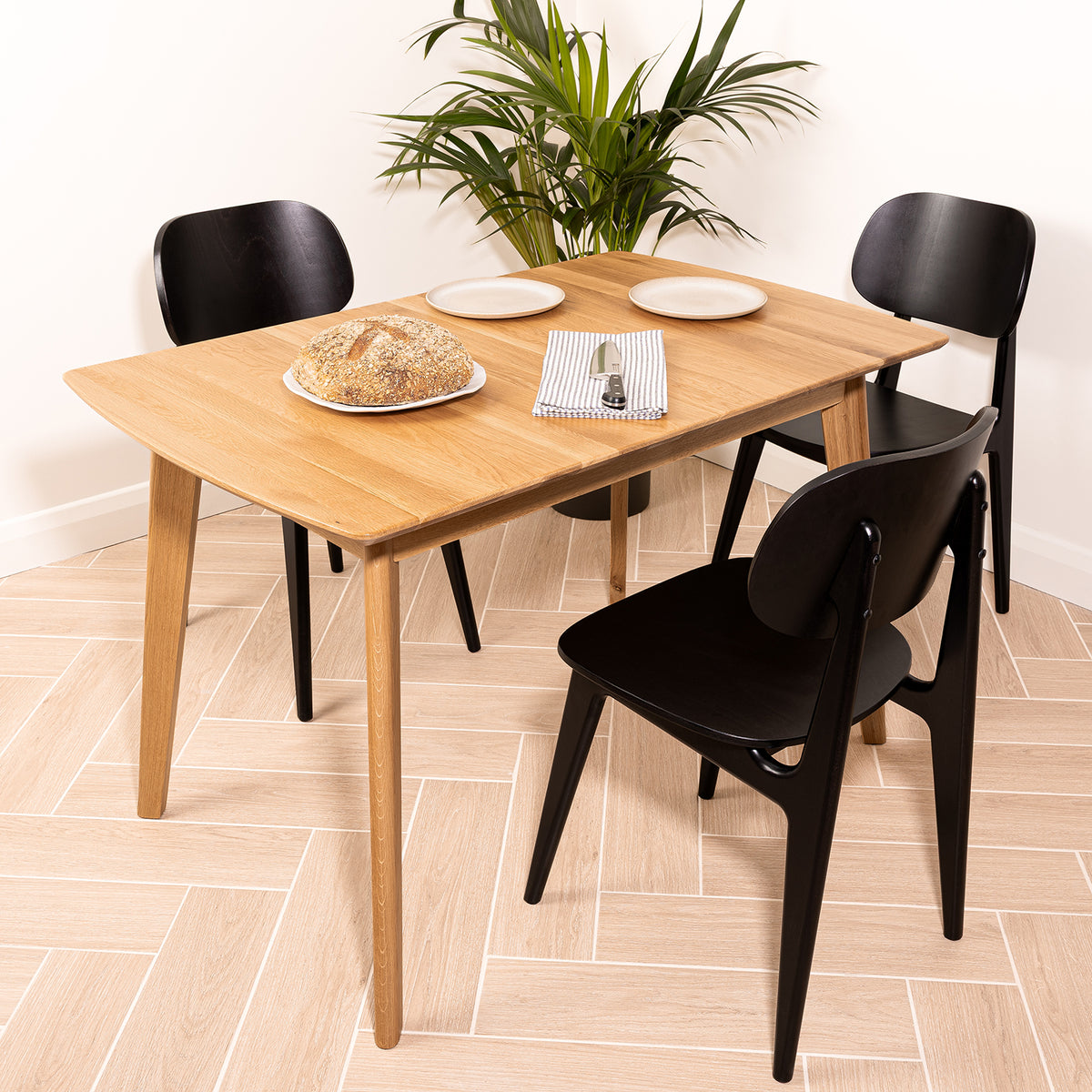 A rectangular Otti wooden oak dining table with tapered oak legs, shown with three chairs in a bright room.
