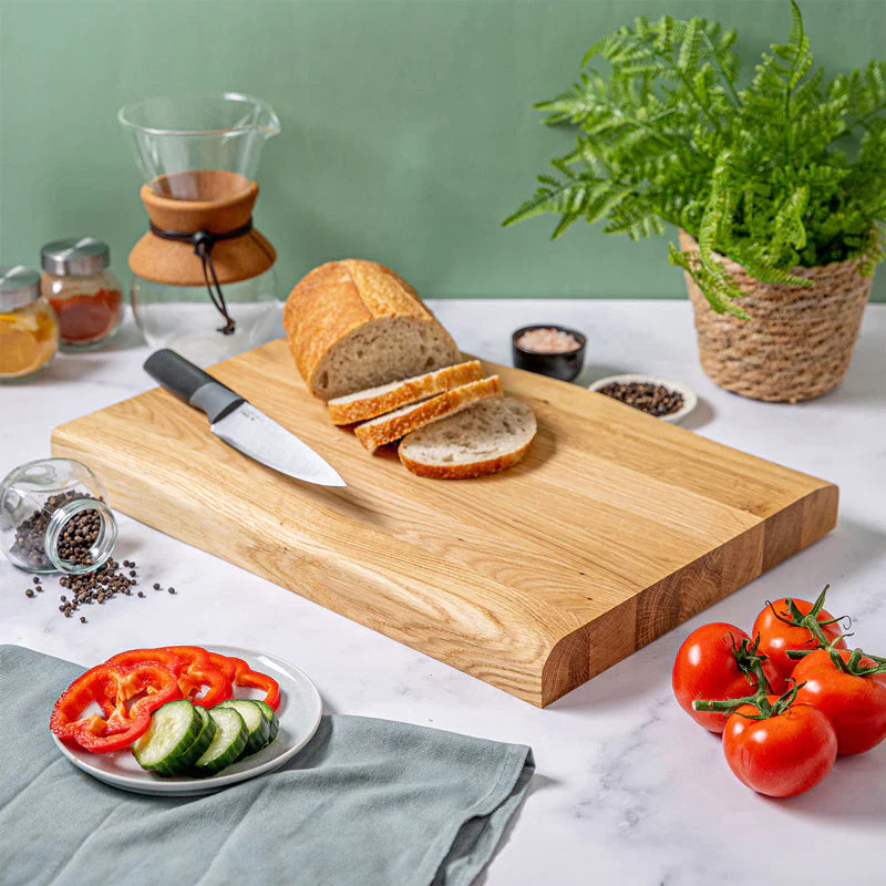 Solid wood chopping board with sliced bread and kitchen accessories.