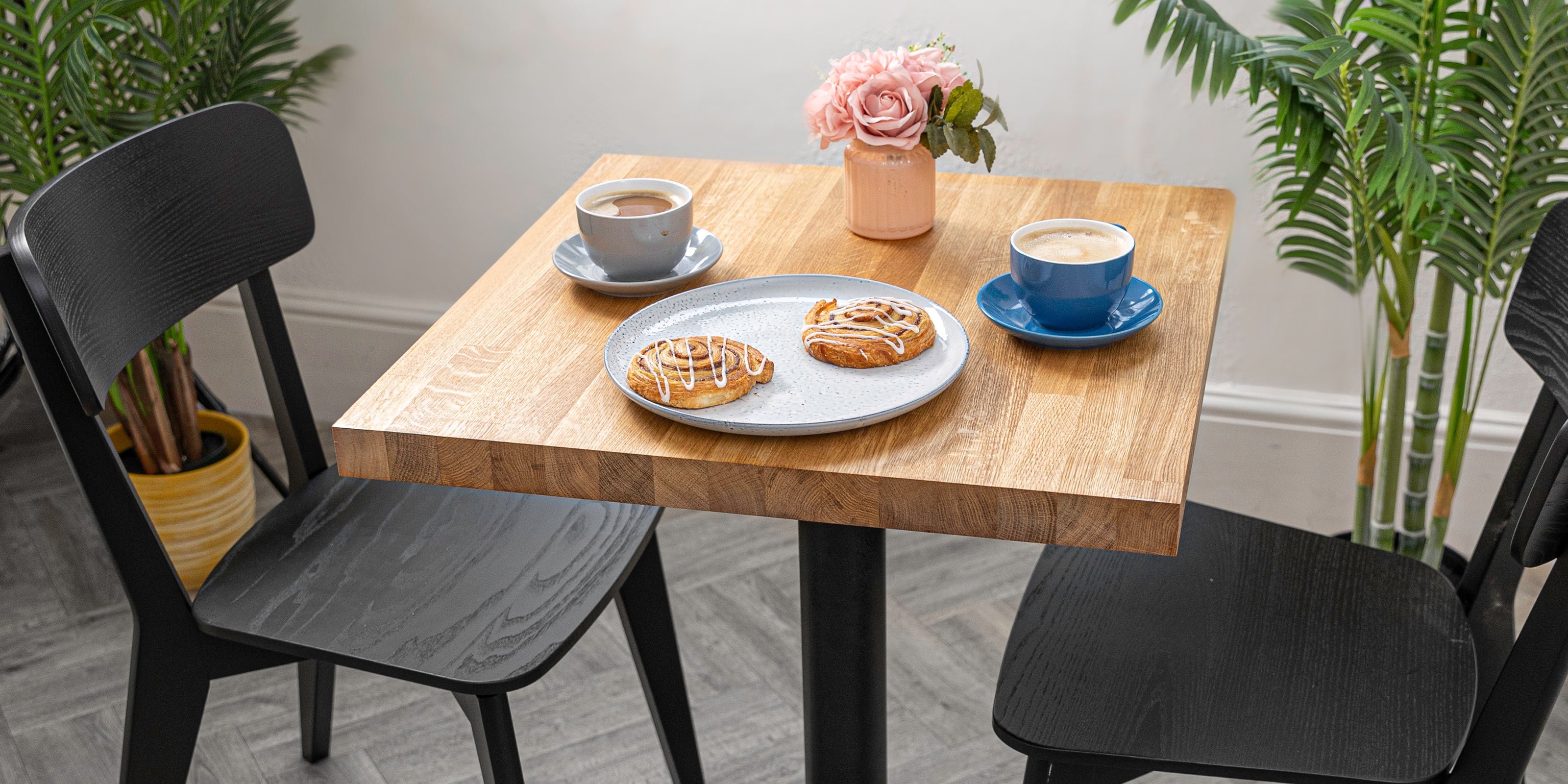 Solid oak bistro table with black dining chairs, set with coffee and pastries.