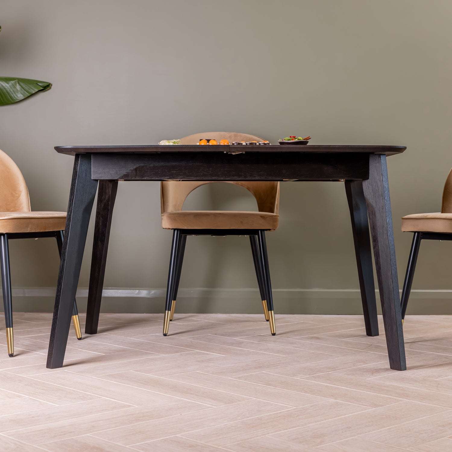 A black oak wood extendable dining table, shown in a styled dining room setting with upholstered chairs against a green wall.