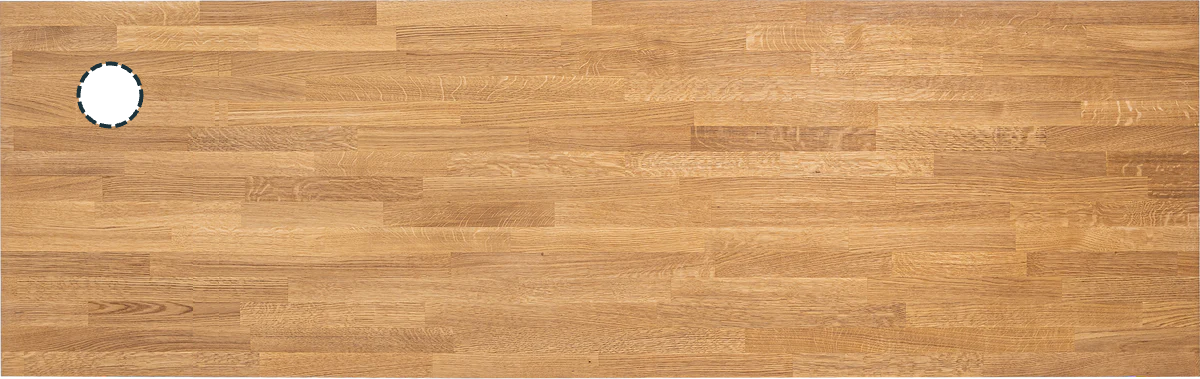 A top view of an oak wood desktop with visible grain and a small circular cable hole cutout.