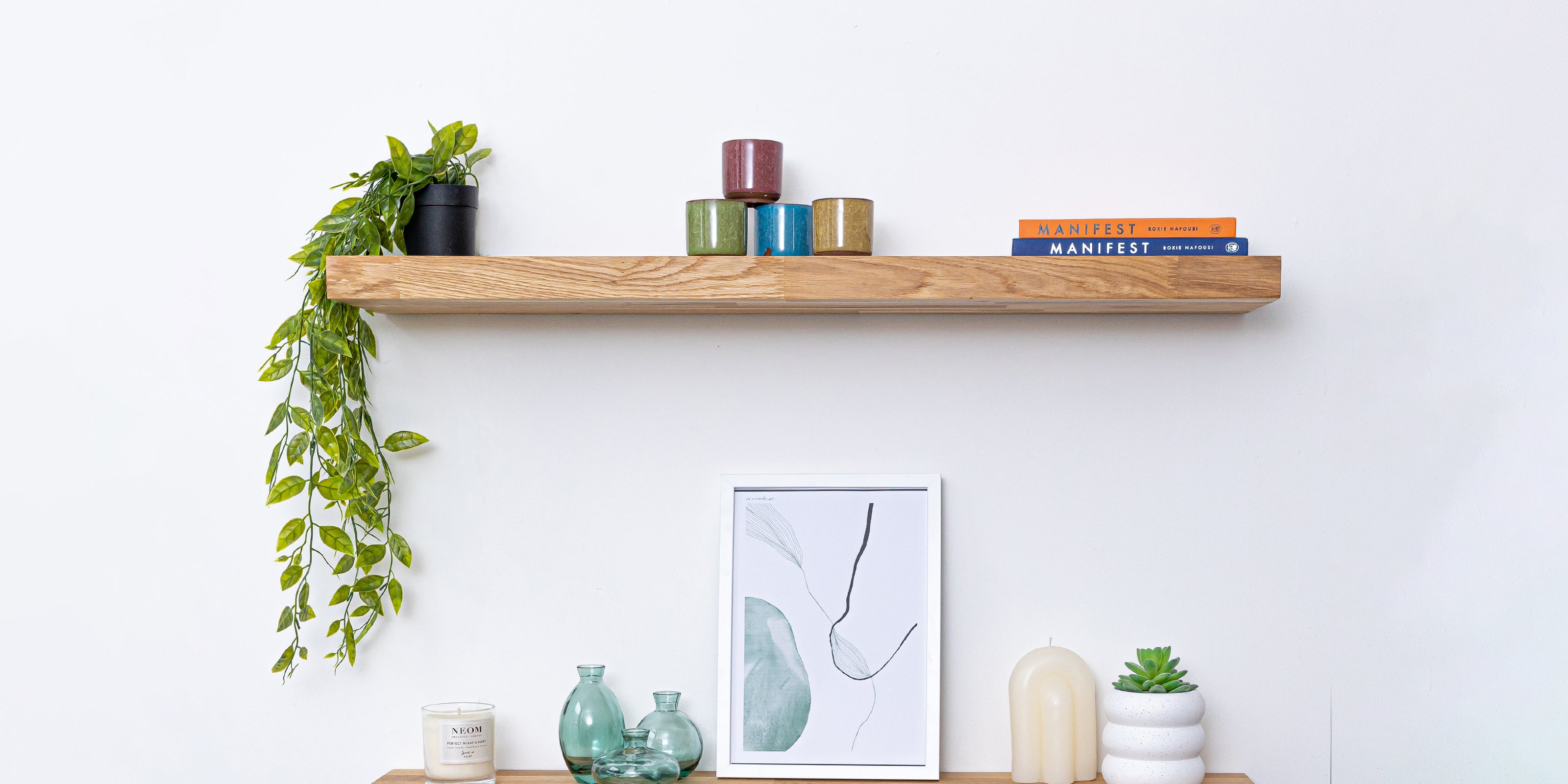 Solid oak floating shelf styled with plants, books, and ceramics.
