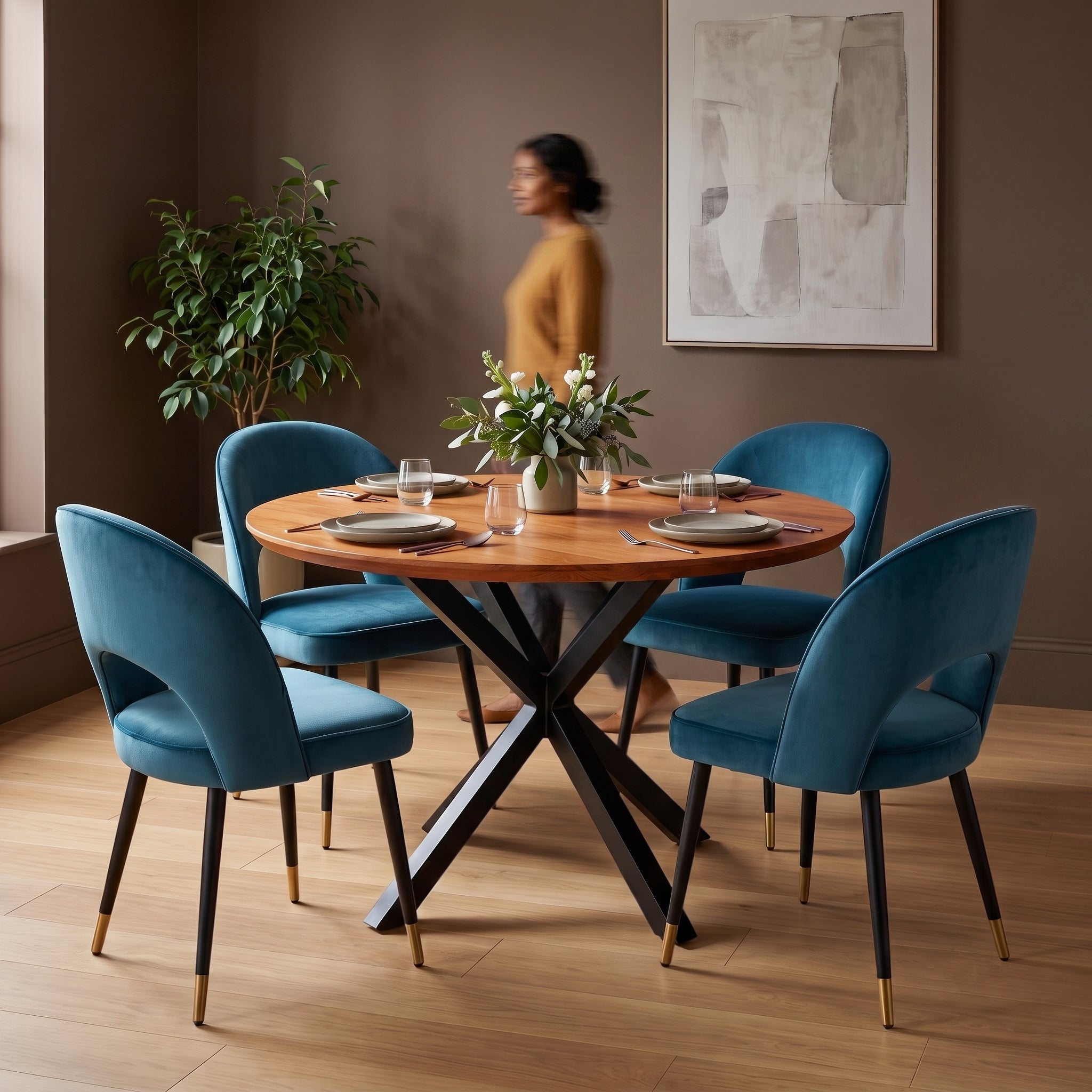 Dining room with a premium round wooden table and blue chairs, featuring a woman in the background.