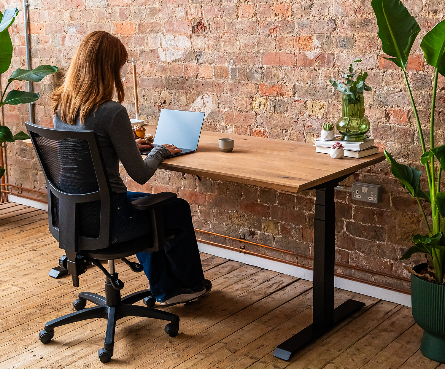 Person seated at a premium solid oak standing desk in a workspace setting.