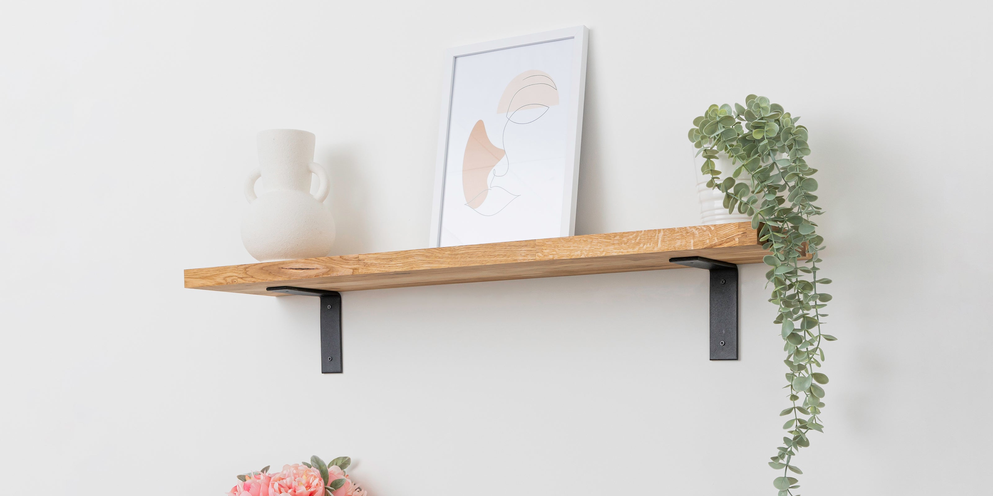 Solid oak wooden shelf with black flat-style brackets and decorated with a plant, vase, and frame.