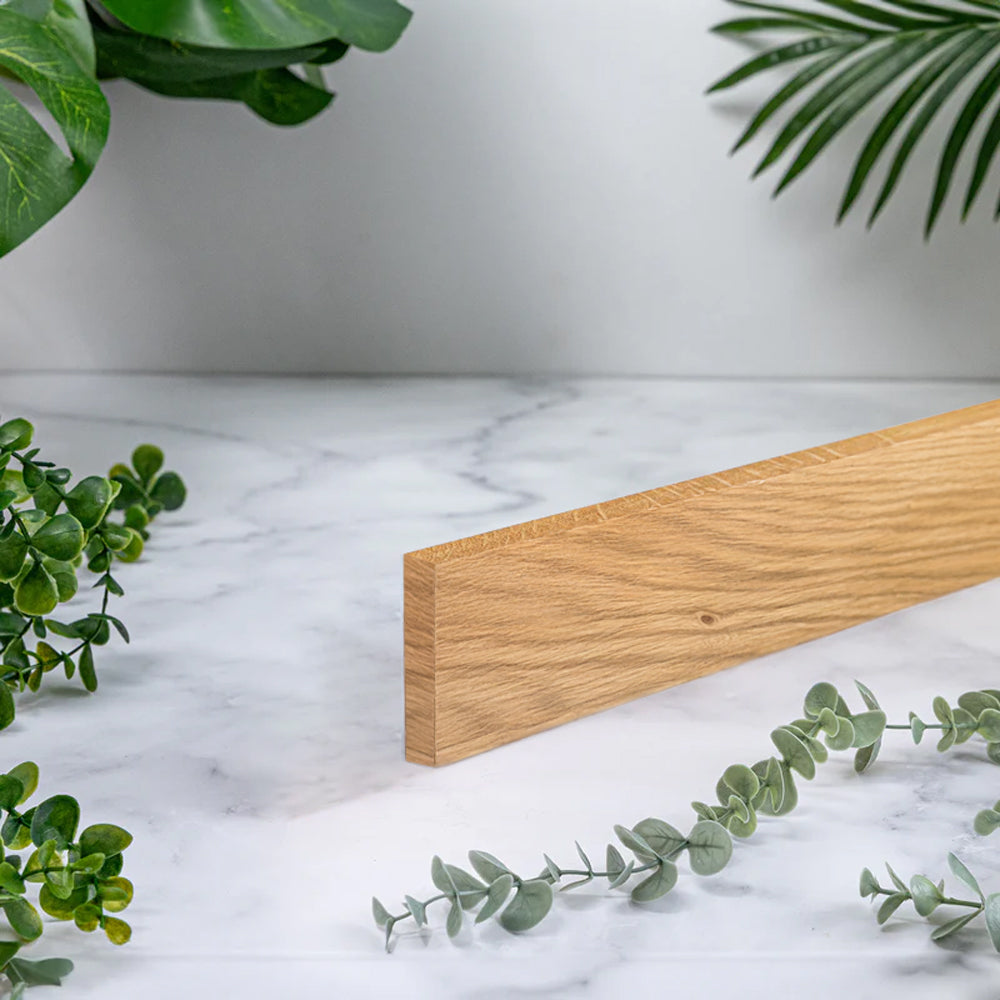A full stave solid oak worktop upstand, photographed on a white marble surface with green plants around it.