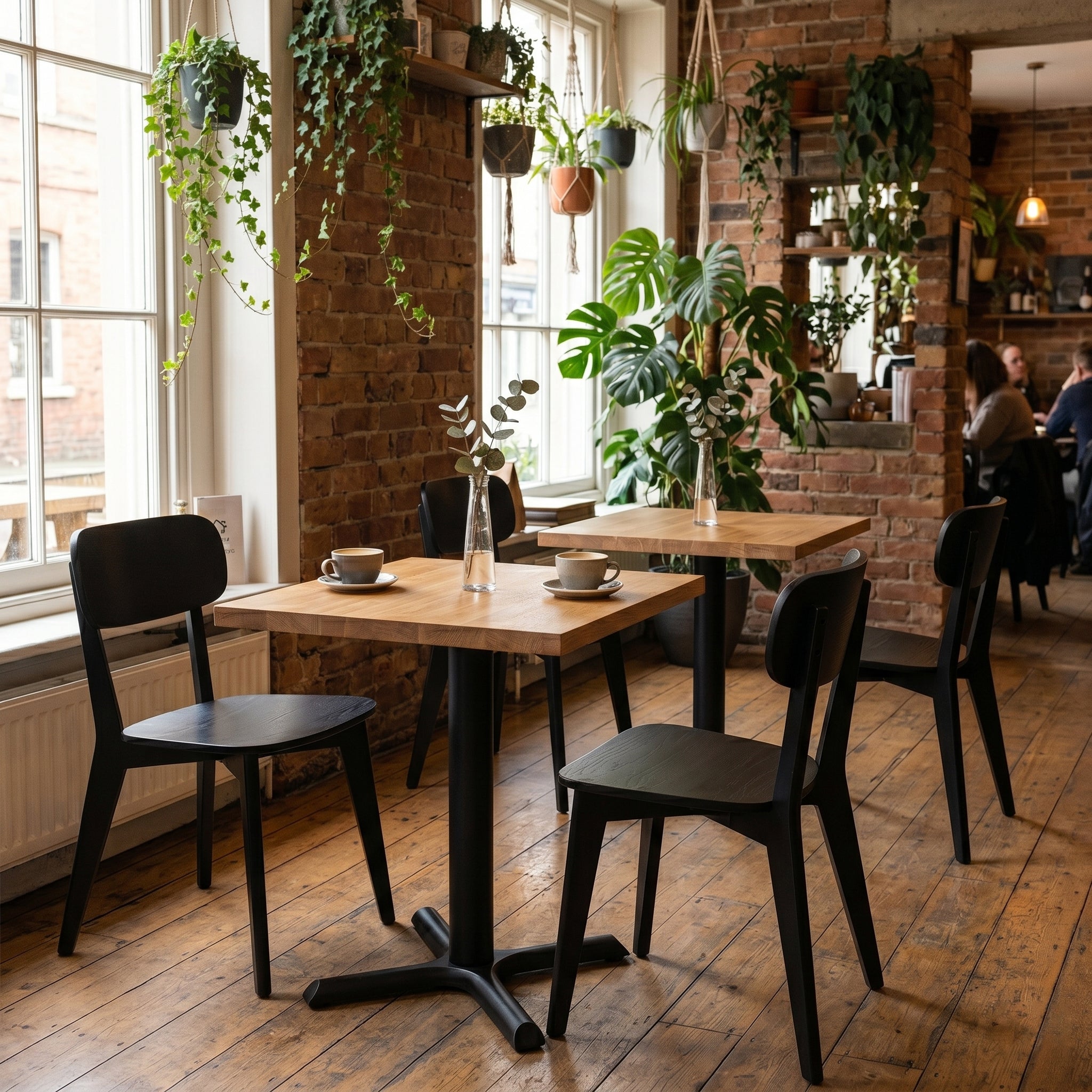 Oak solid wood bistro tables shown in a cafe setting with rustic flooring, brick walls and hanging plants. 