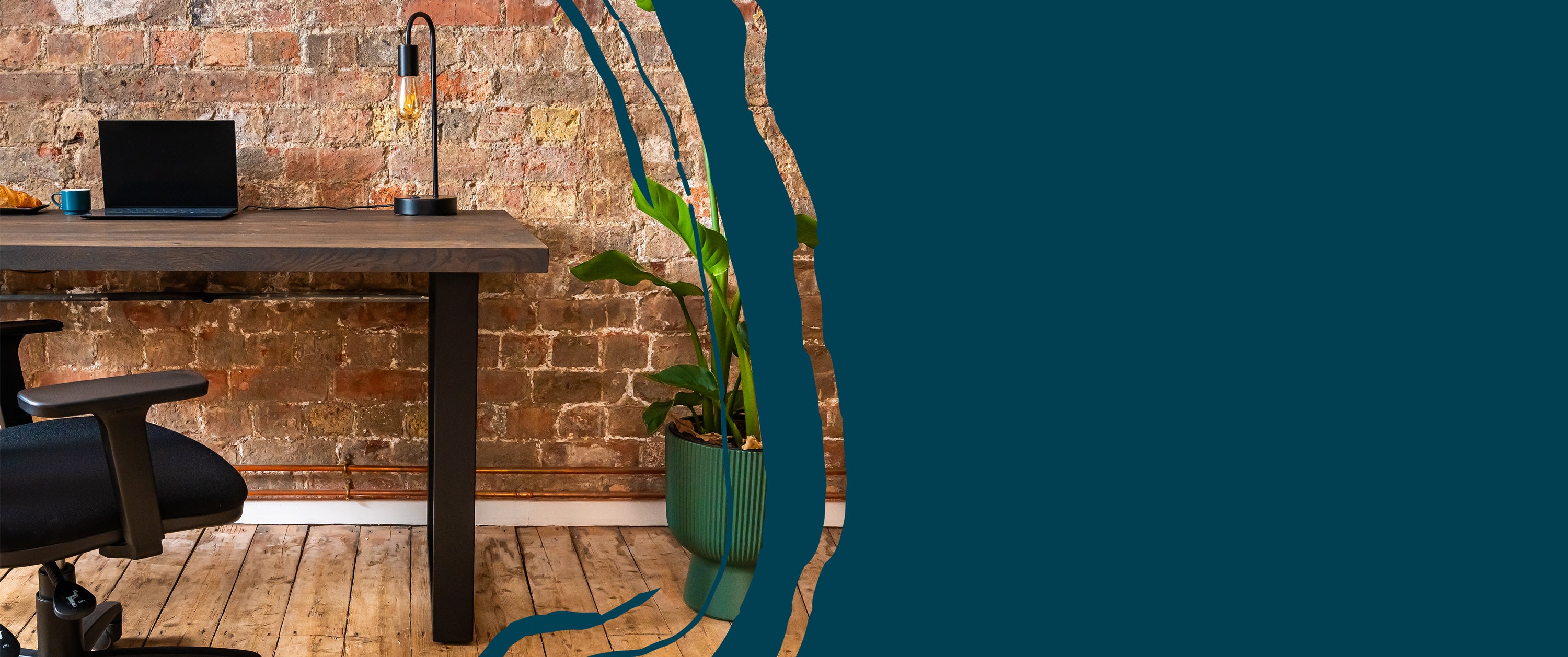 Solid wood desk shown in a natural office setting with chair and potted plant.