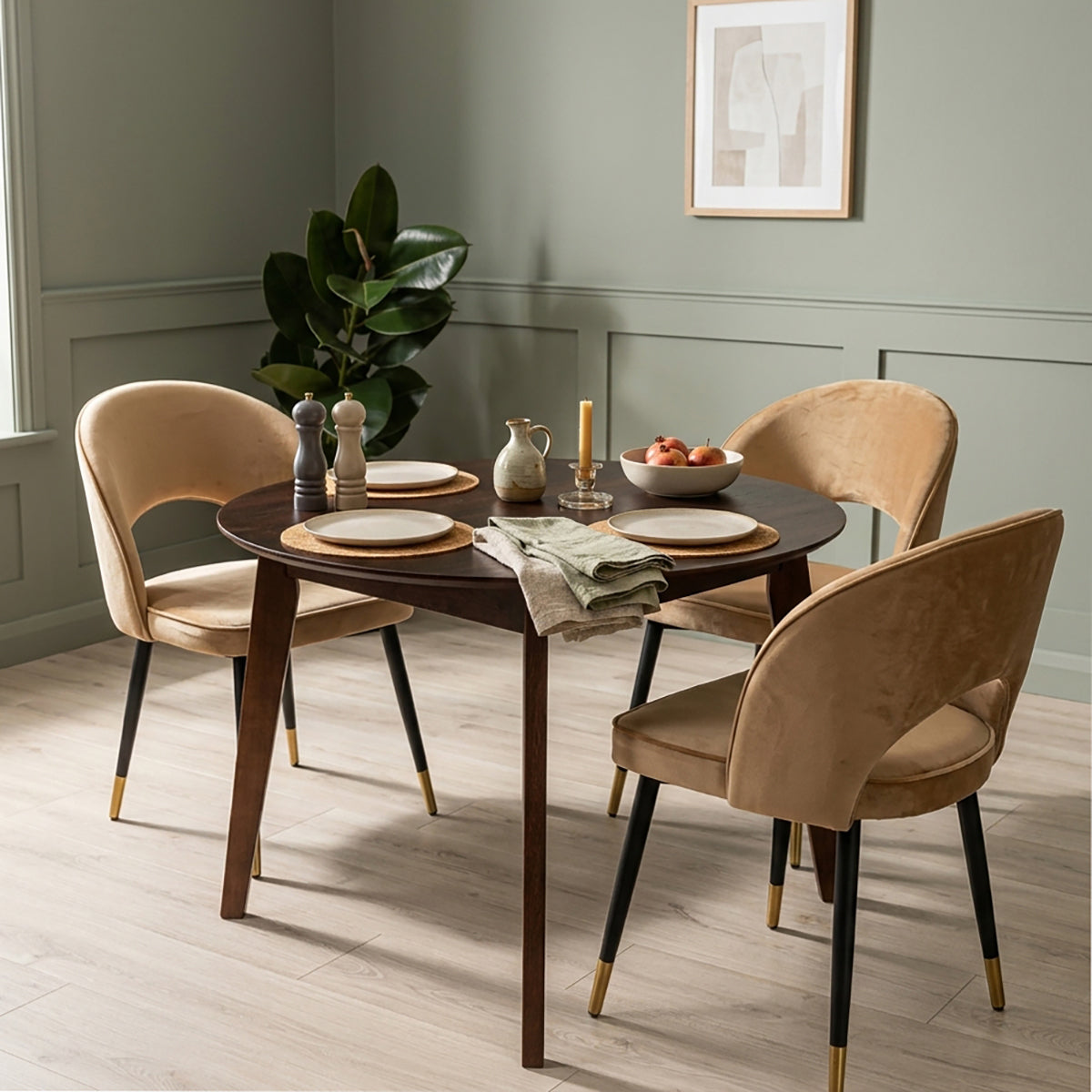 A dining set featuring a walnut effect oak round wooden table and three velvet dining chairs with black champagne-capped feet, styled in a modern dining room with sage green walls.