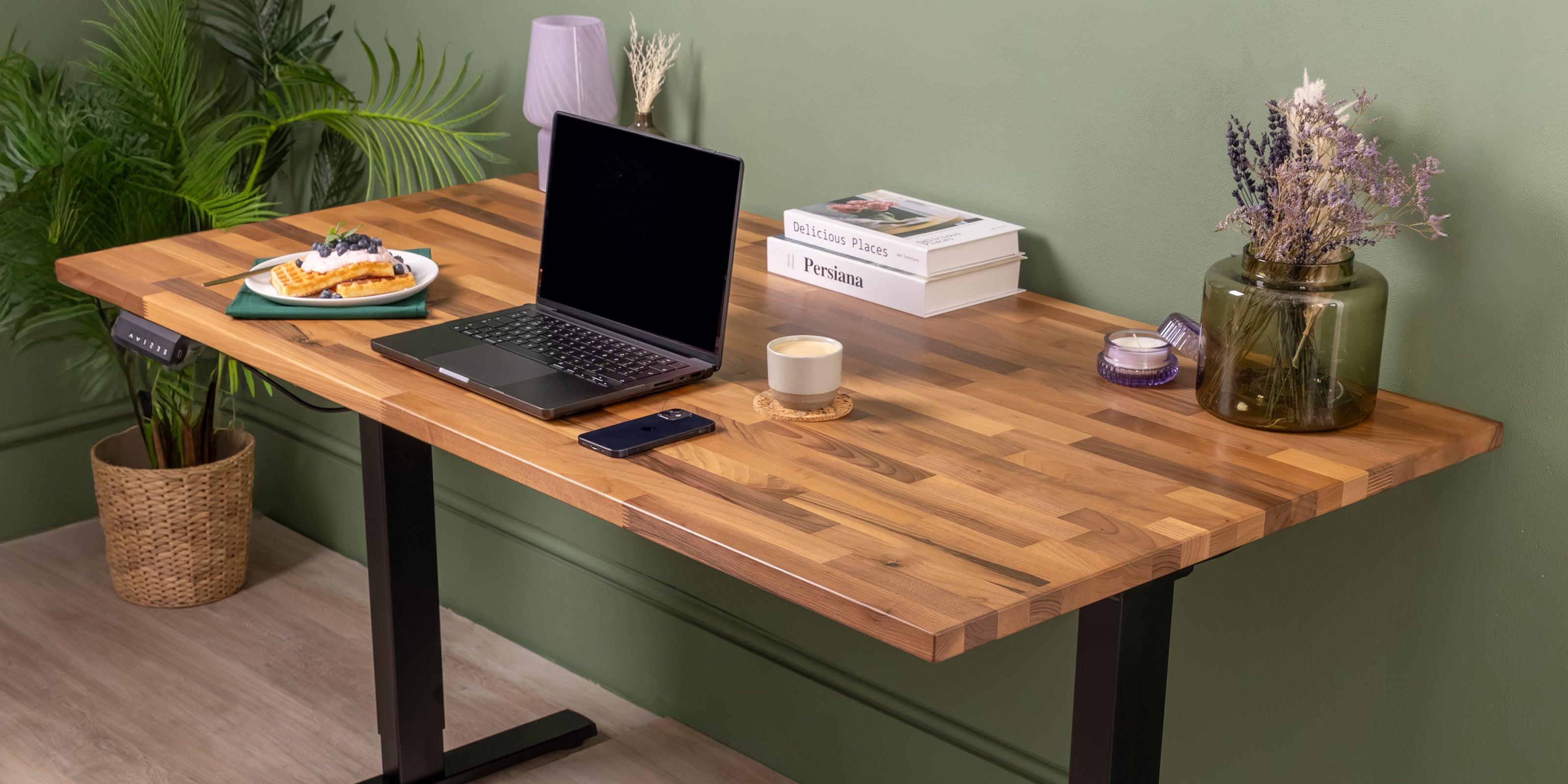 Walnut solid wood desk on a black d2 standing desk frame with books, flowers, food and a drink.
