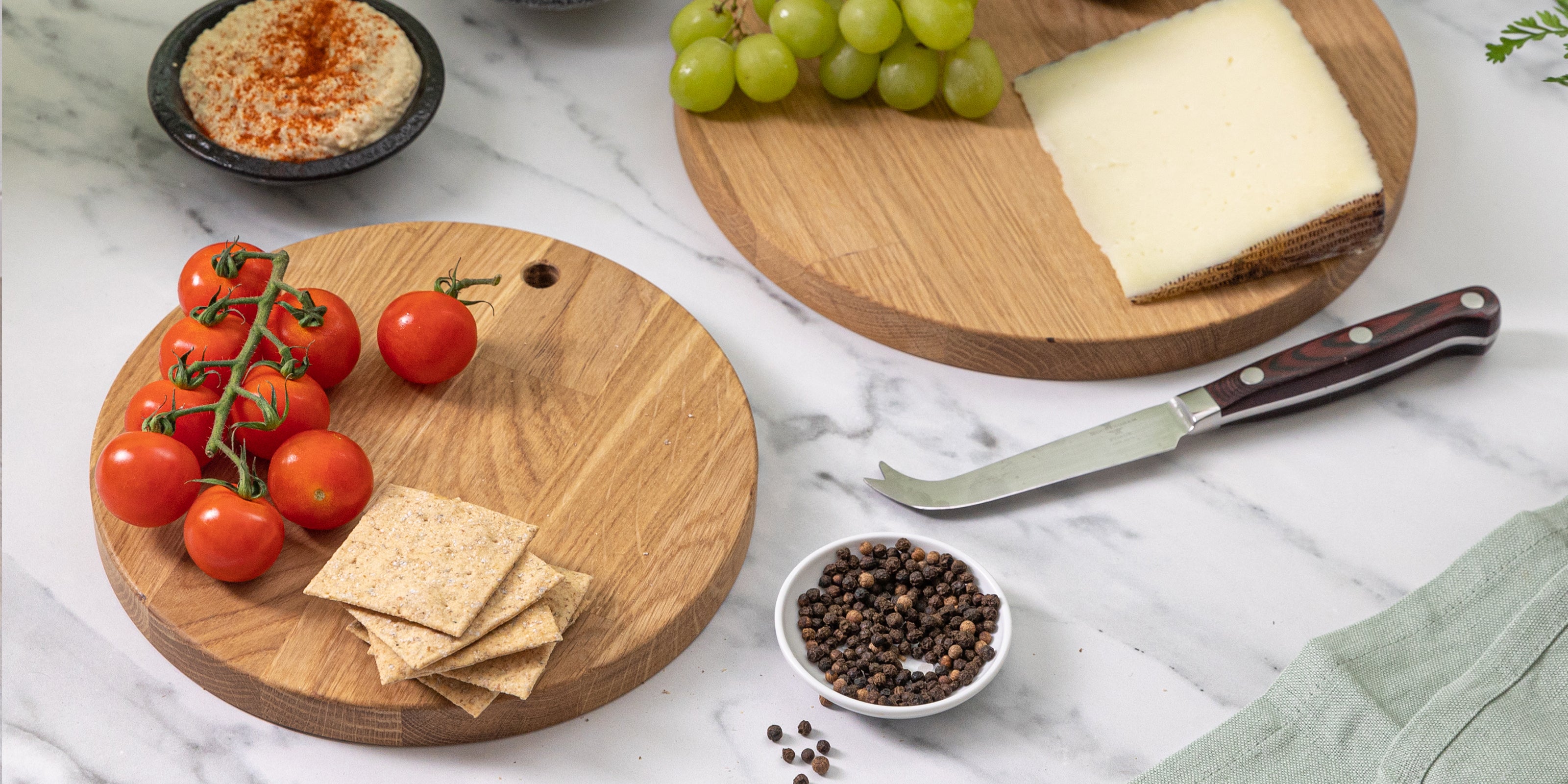 Wooden serving boards with tomatoes, crackers, and a knife on a marble surface.